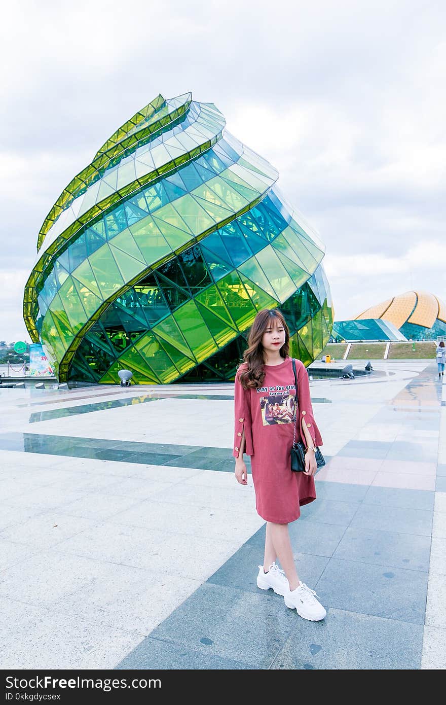 Woman in Red Long-sleeved Top Wearing White Sneakers Walking in Front of Green and Blue Glass Building