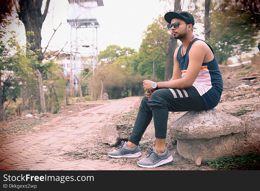 Man Wearing Black Tank Top Sitting on Gray Stone