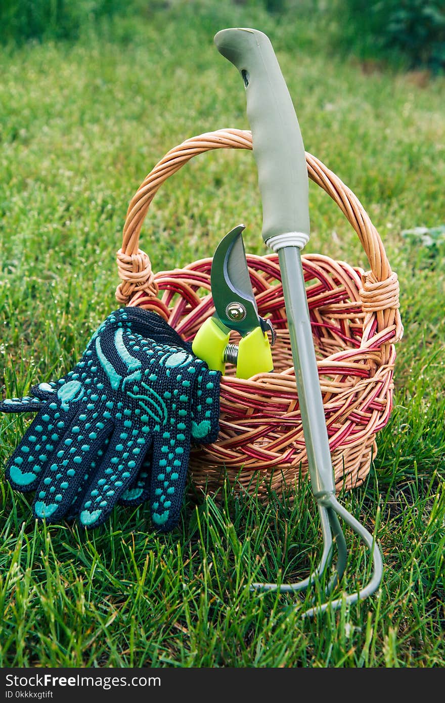 Small hand garden rake, pruner and gloves with wicker basket in green grass. Garden tools and equipment