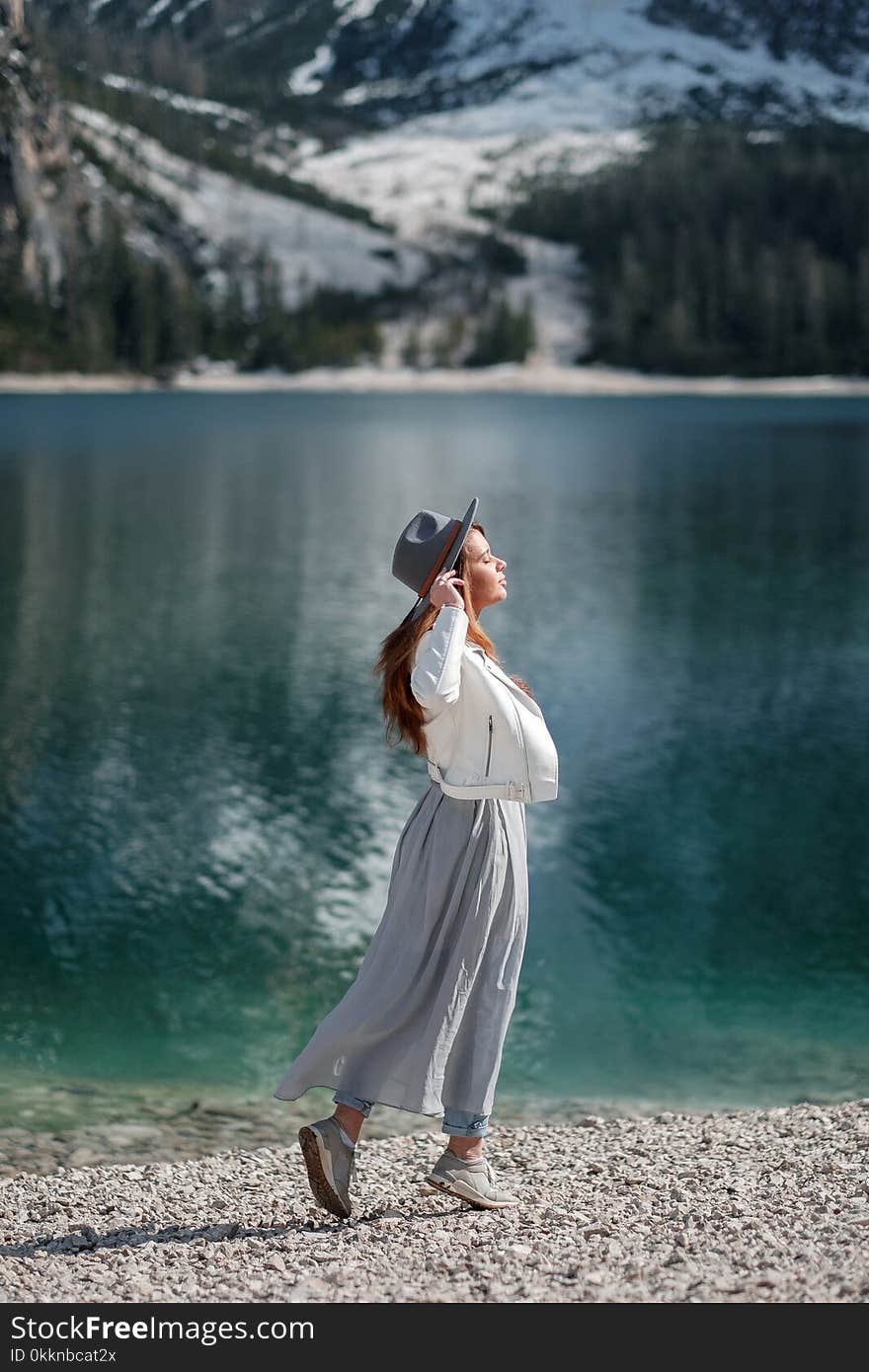 A girl in a hat and a long dress is walking along the lake. Lago di Bries in the north of Italy