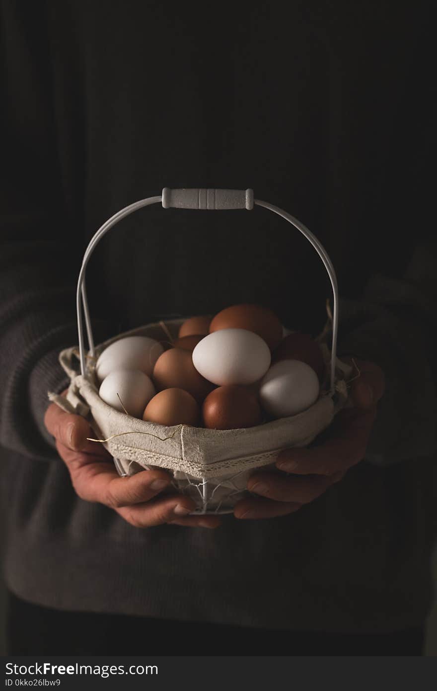 Man`s hands holding a basket with fresh brown and white chicken eggs over dark background