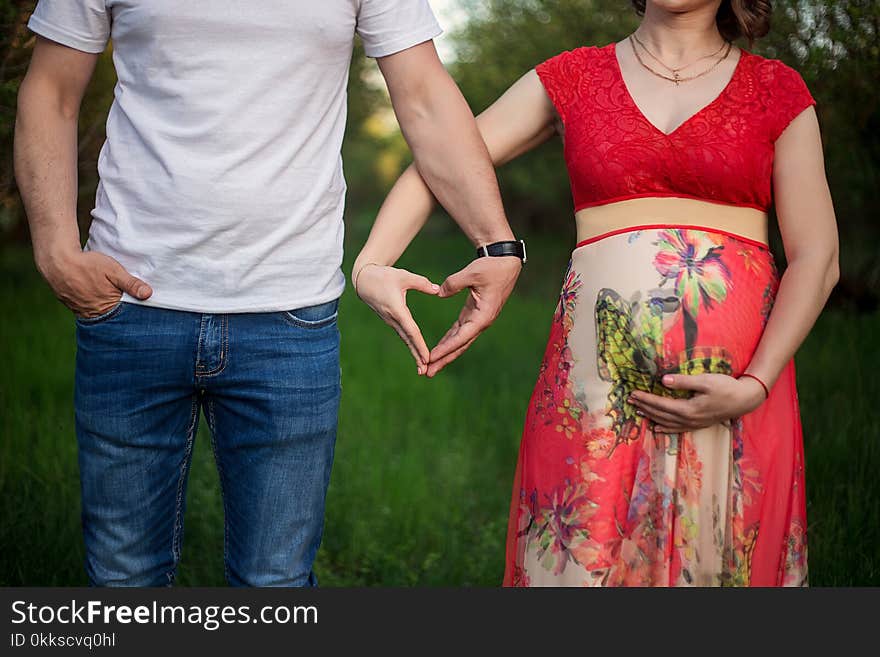 A happy pregnant couple made from hands made of a heart on a background of green grass in the park.