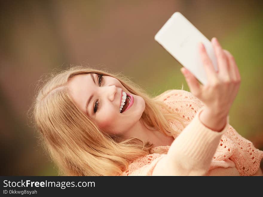 Nature outdoor internet technology concept. Cheerful blonde girl taking selfie. Young gorgeous lady takes picture of herself in autumnal forest.