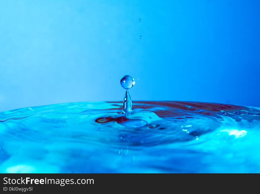 Drop of water falling in blue water and blue background.