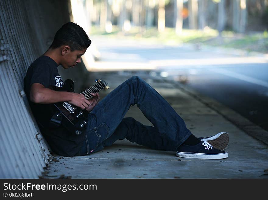 Man Sitting Near Wall Playing Guitar