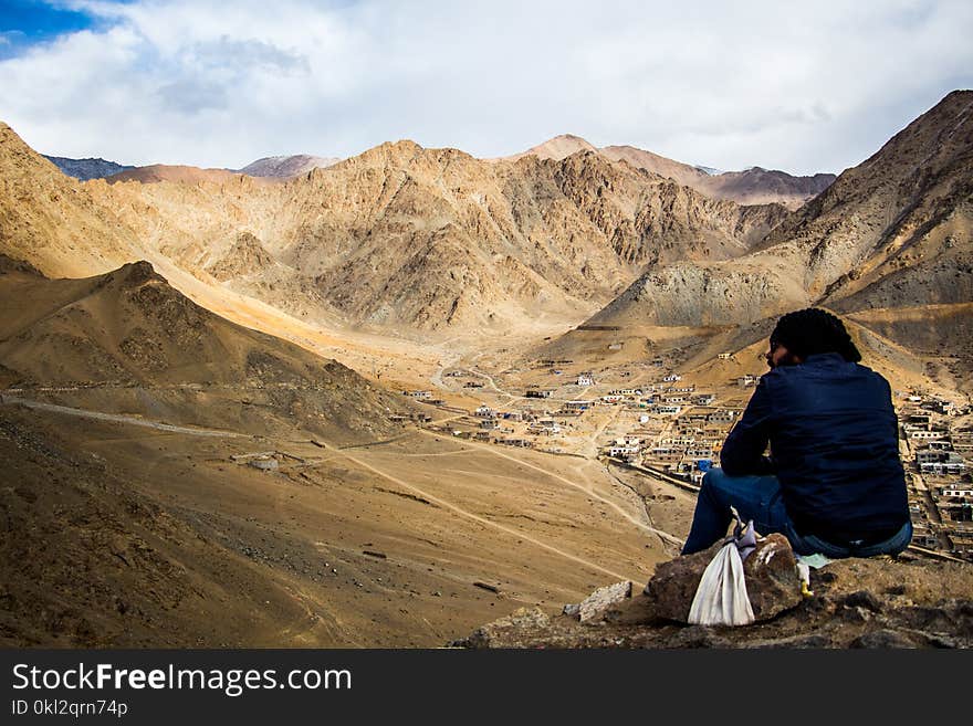 Person Sitting on Mountain Under White Sky