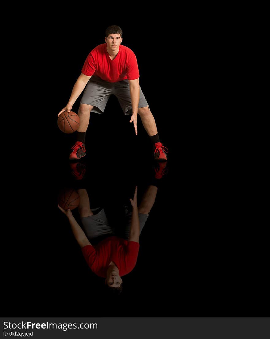 Young athlete in red tee shirt playing basketball on reflective, black surface. Young athlete in red tee shirt playing basketball on reflective, black surface