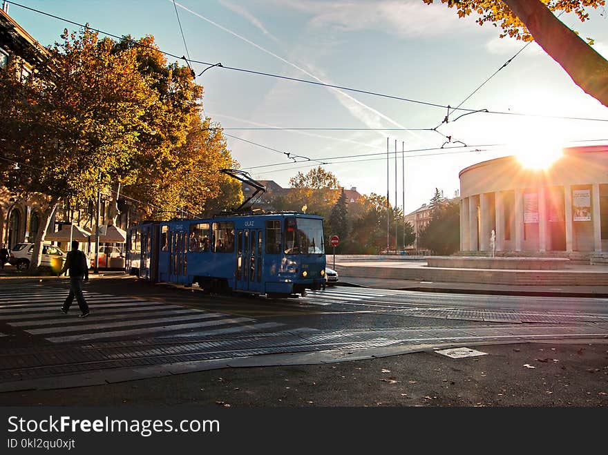 Person Wearing Black Walking on Pedestrian Lane Near Blue Tram Train during Sunset