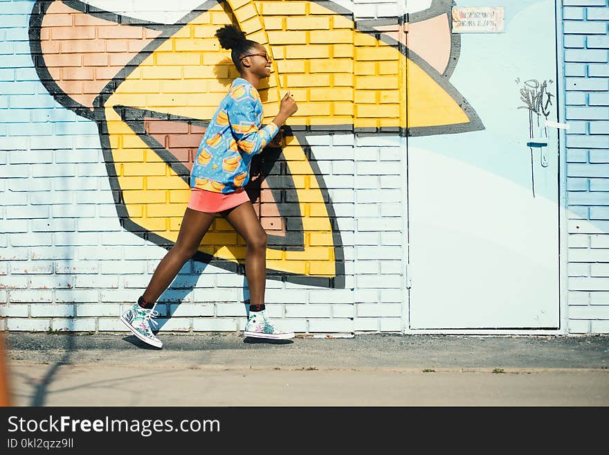 Woman Wearing Blue and Yellow Long-sleeved Shirt Walking Near White and Yellow Painted Wall