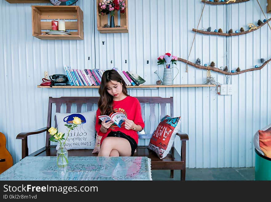 Woman in Red Shirt Reading Book While Sitting on Bench