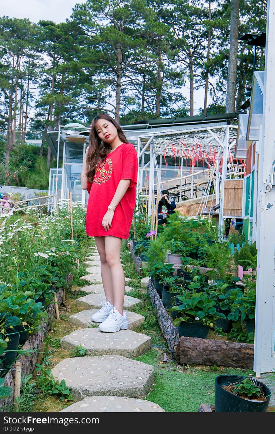 Woman Wearing Red Crew-neck Shirt Standing Between Plants Near Trees