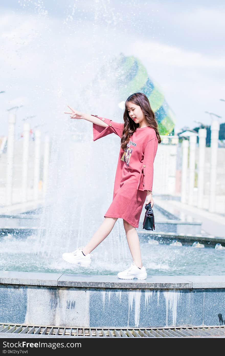 Woman Wearing Pink Long-sleeved Dress Walking on Fountain during Daytinme