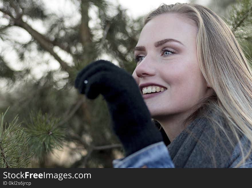 Woman Wearing Grey Scarf Holding a Pine Leaf While Smiling