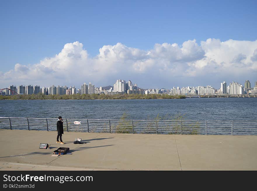 Person Standing on Gray Road Beside Body of Water