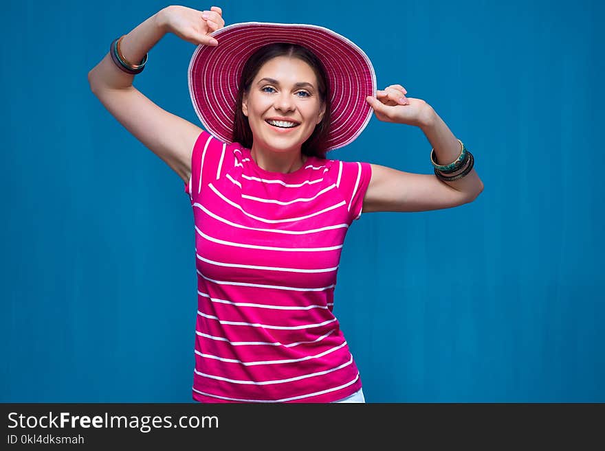 Smiling young woman wearing pink beach hat posing against blue background.