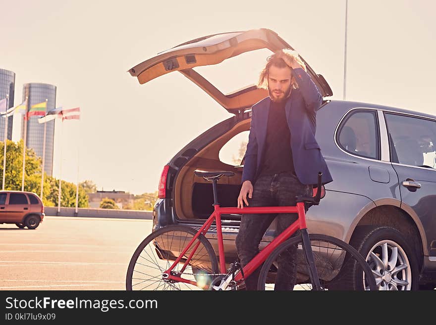 A man holds fixed bicycle near the car with open trunk.