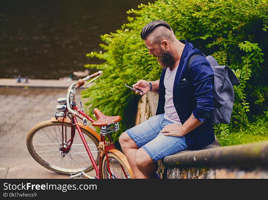 Casual bearded male in a park talks by smart phone.