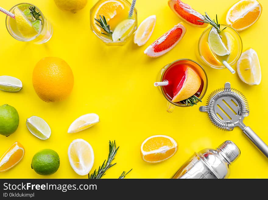 Mix exotic fruit cocktail with alcohol. Shaker and strainer near citrus fruits and glass with cocktail on yellow background top view.