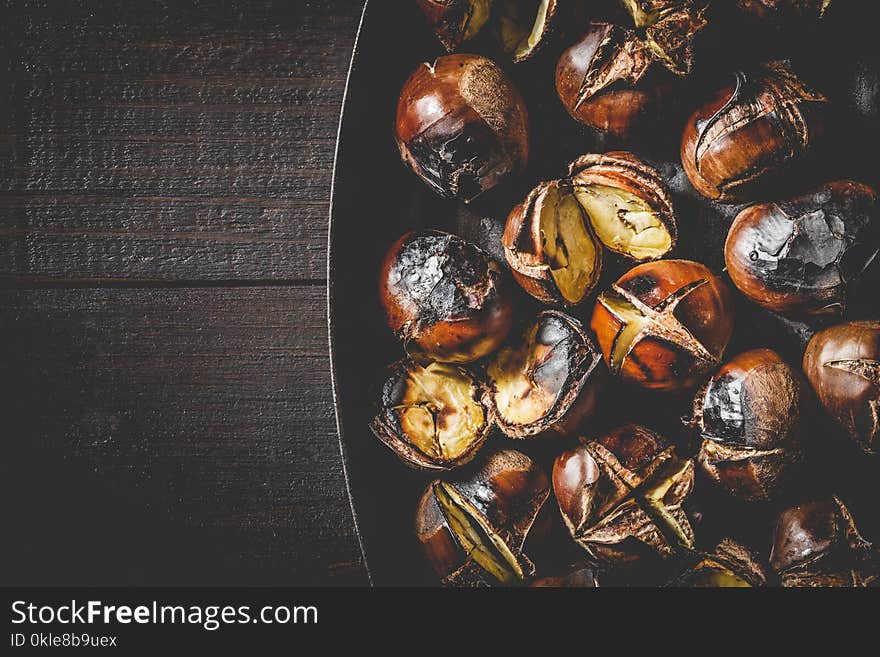 Close up of Roasted chestnuts in iron grilling pan over rustic wooden table, top view, copy space.