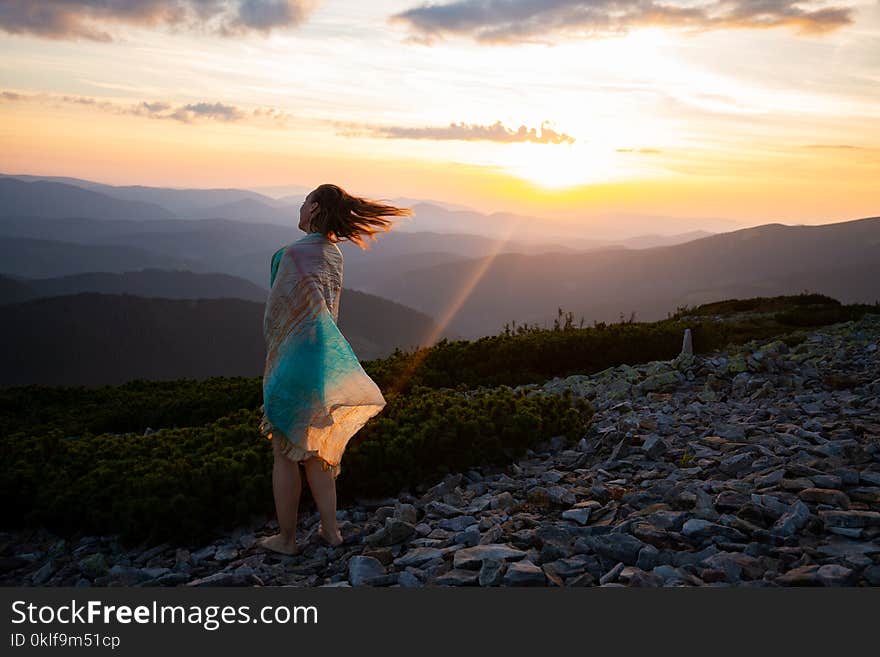 Romantic woman in a scarf stands on the top during sunset