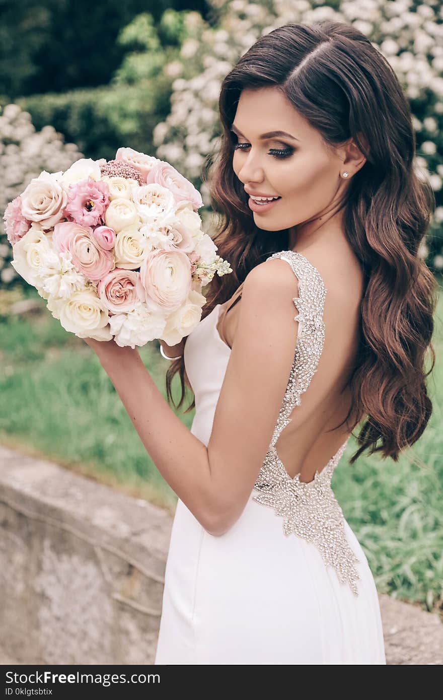 Beautiful bride with dark hair in luxurious wedding dress with tender wedding bouquet