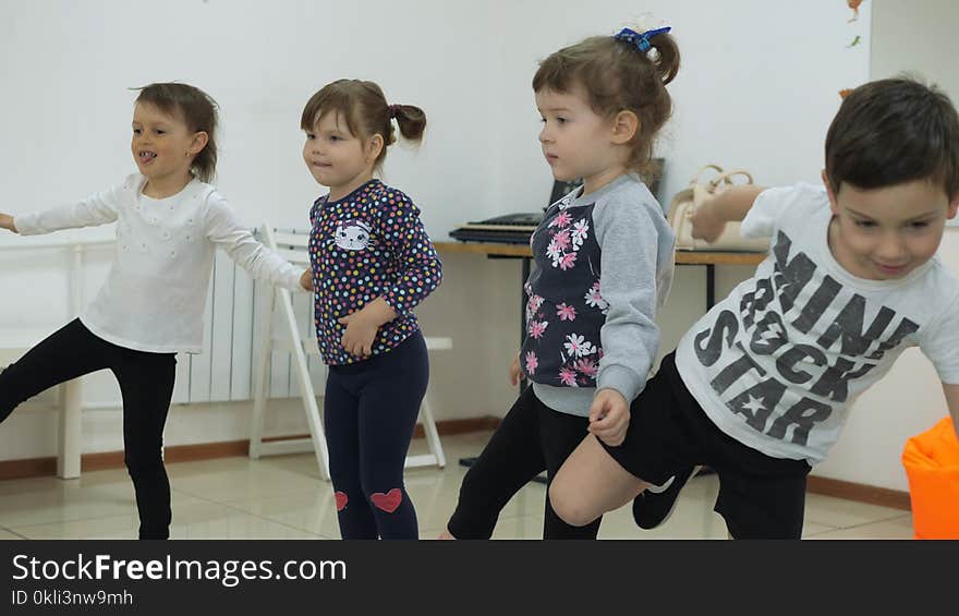 Children`s developing a game room. Emotions of young children during entertaining classes. The guys stand in line stepping from foot to foot. Children raise one leg high and keep balance.