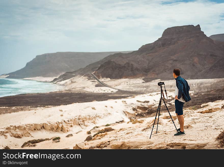 Photographer with camera in desert admitting unique landscape of sand dunes volcanic cliffs on the Atlantic coast. Baia