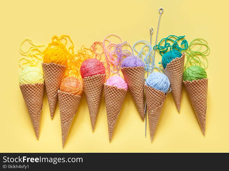 Balls of yarn lie in a waffle cone for ice cream. Coloured wool. yellow background