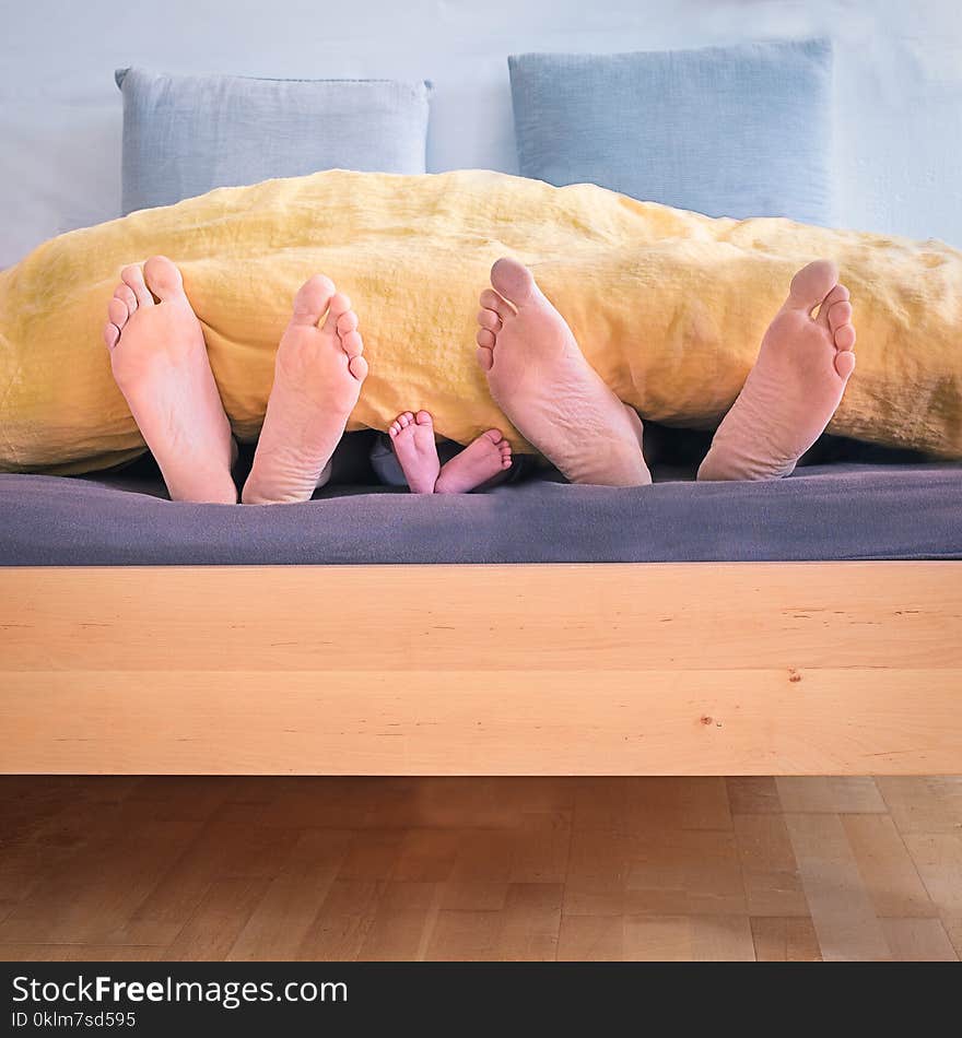 Family of Three Lying on Bed Showing Feet While Covered With Yellow Blanket