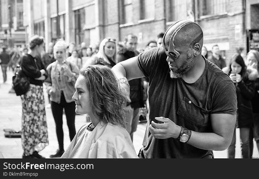 Grayscale Photography of Man Cutting Hair of Woman Surrounded With People