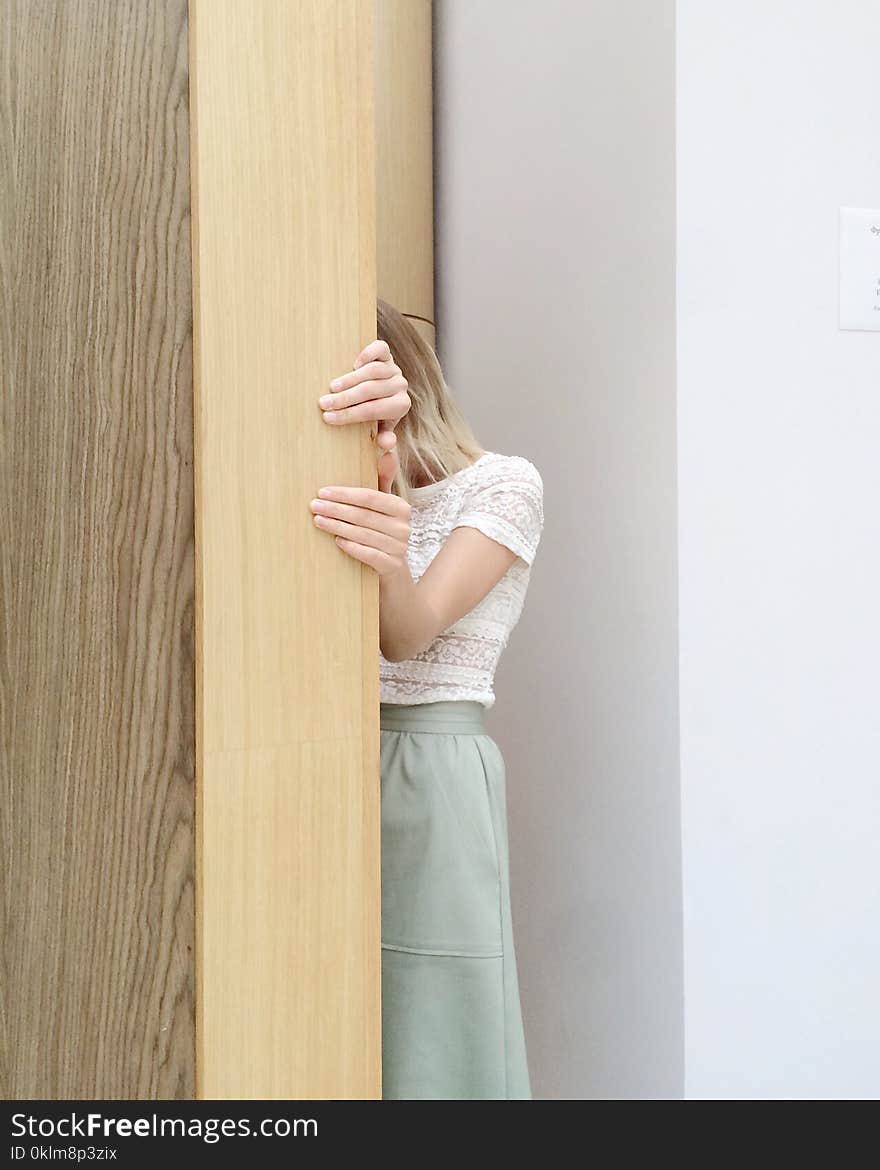 Woman in White Lace Cap-sleeved Top and Green Skirt Hiding Behind Brown Wall