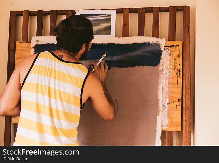 Man in White and Yellow Stripe Tank Top Painting on Canvas