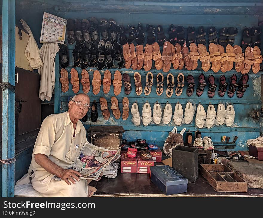 Man Reading Newspaper Surrounded by Shoes