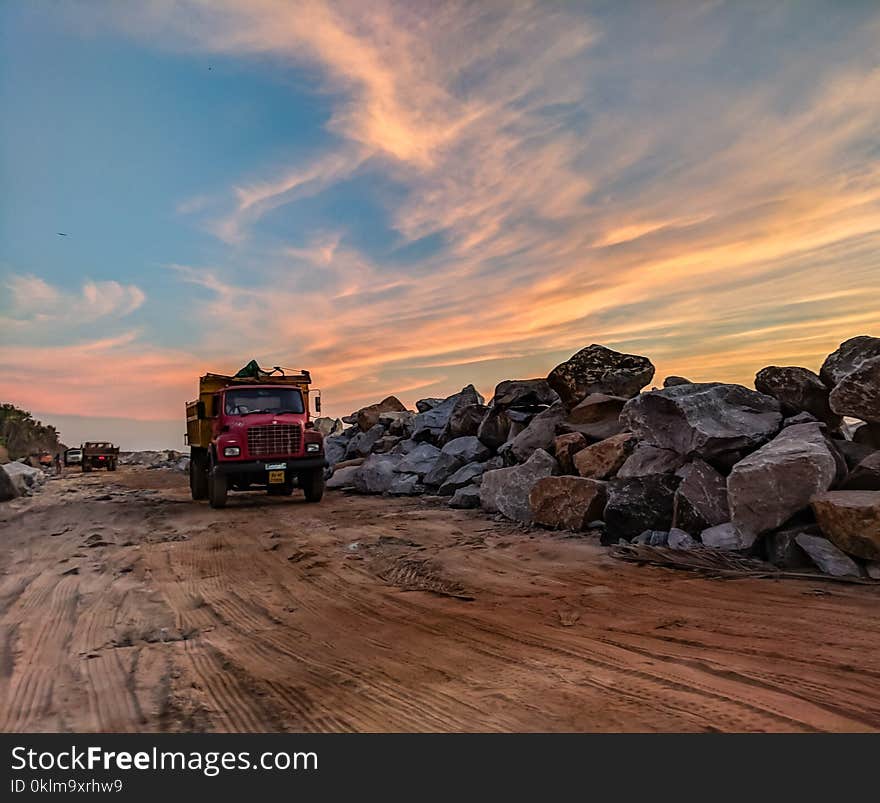 Red Dump Truck Near Filed Rocks Under Cloudy Sky