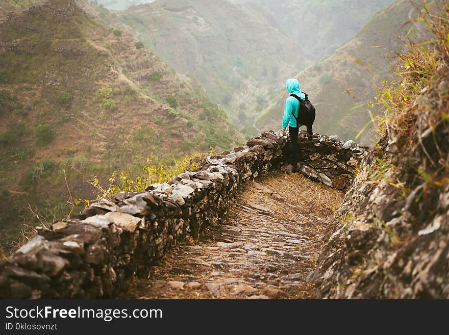 Hiker with backpack on the mountain edge cobbled path looking down the valley. Rocky terrain of high mountain ranges and