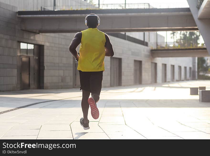 Young fit man in yellow t-shirt running sunset outdoors, autumn running, attractive dark skinned runner jogging fast in the park with beautiful light on background, sport concept. Young fit man in yellow t-shirt running sunset outdoors, autumn running, attractive dark skinned runner jogging fast in the park with beautiful light on background, sport concept