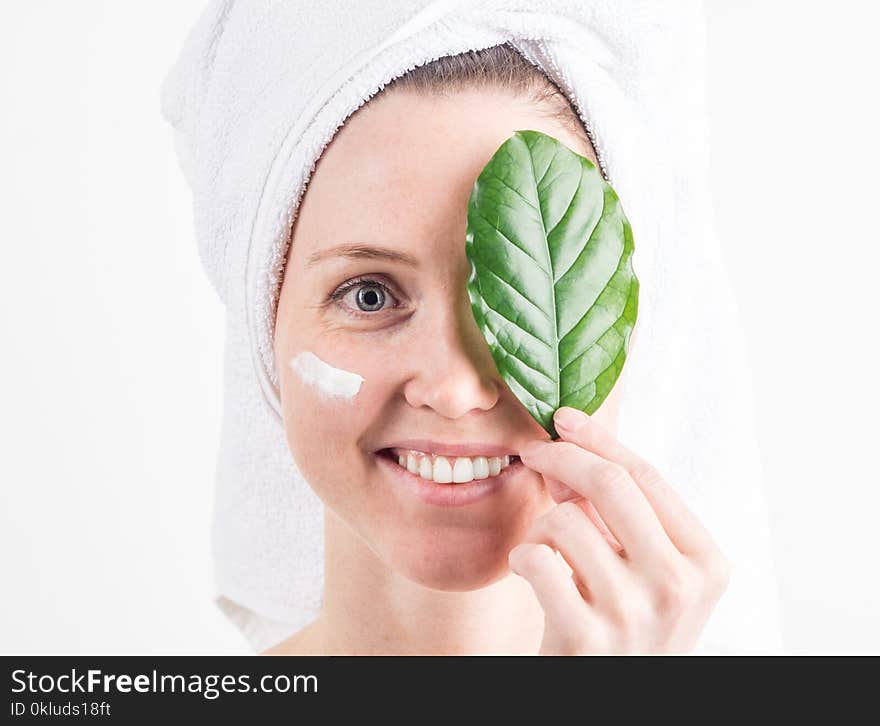 Natural Cosmetics: a girl with a white towel on her head smiles and covers one eye with a green leaf.