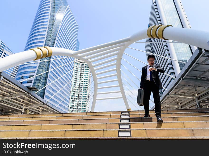 The Asian Businessman Has Holding A Black Bag And Looking On Watch In Hurrying Time.