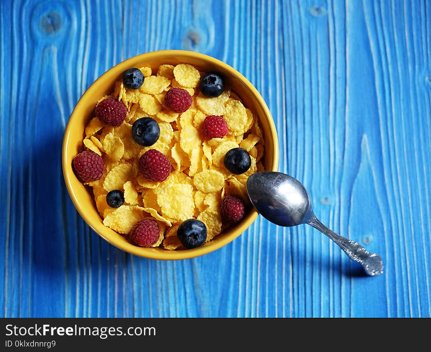 Cornflakes with berries raspberries and blueberries on blue wooden background.