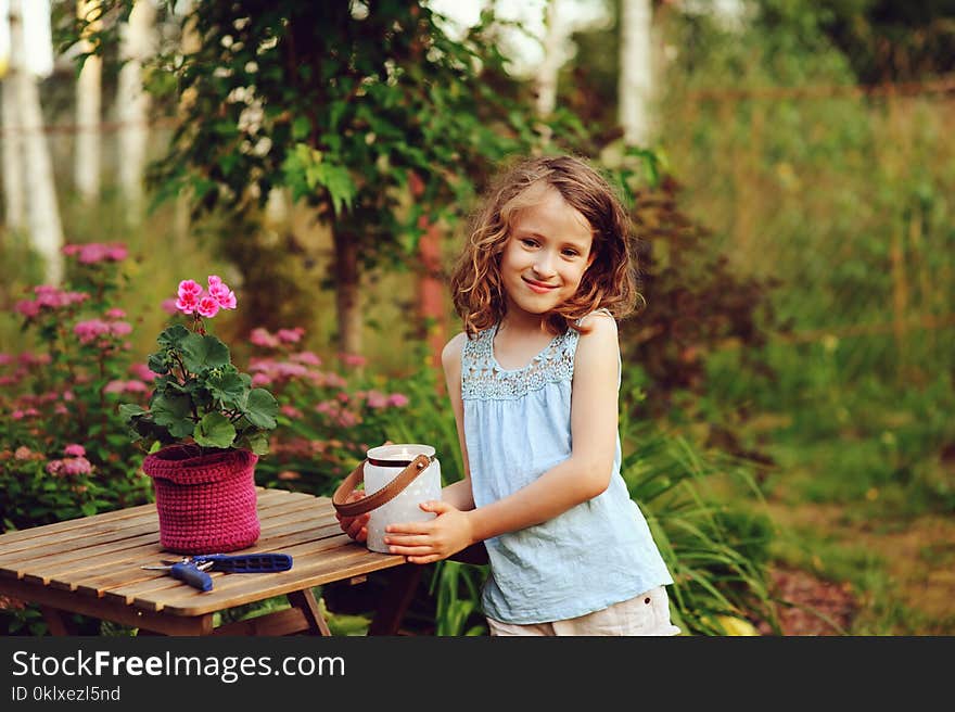 Happy child girl decorating evening summer garden with candle holder. Smiling kid helps on backyard on vacations