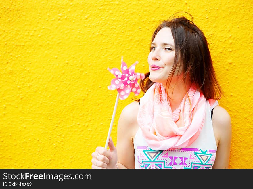 Young woman standing at yellow wall with pinwheel