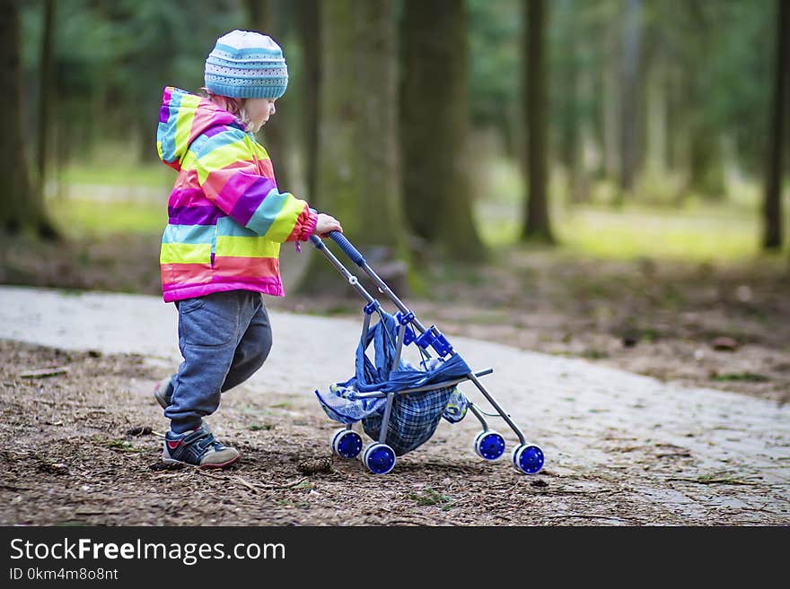 A little girl is rolling toy baby carriage in the park. Child in the park playing with pram.