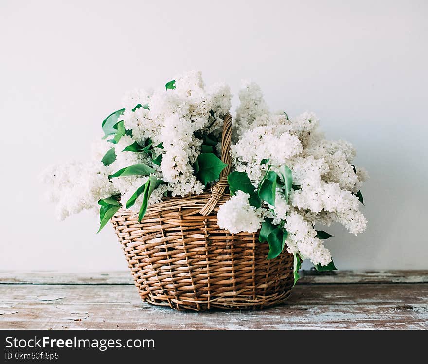 Bouquet of fresh white lilac flowers in wicker basket on wooden