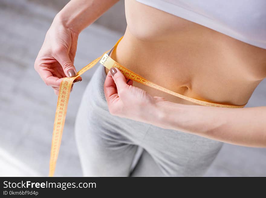 Waist size. Nice slim woman holding a centimeter tape while measuring her waist. Waist size. Nice slim woman holding a centimeter tape while measuring her waist