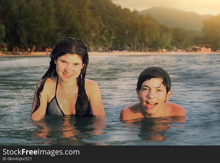 Teenager siblings couple brother and sister swimming in the sea on palm beach background