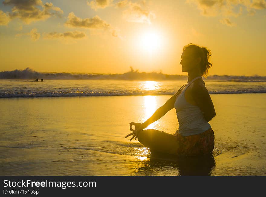 Silhouette of young fit and attractive sport woman in beach sunset yoga practice workout sitting on wet sun in front of sea in meditation and relaxation exercise in mind body care lifestyle