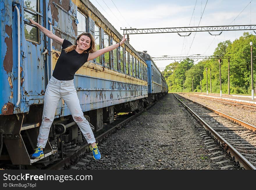 A young beautiful girl is standing on the step of an old railway carriage, a departing train