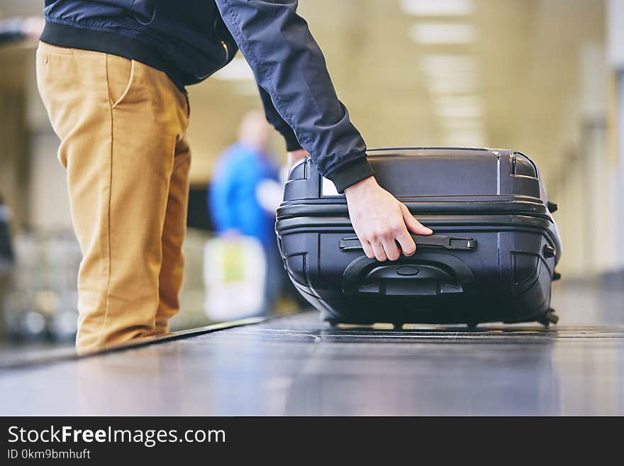 Traveler picking up suitcase from baggage claim in airport terminal. Traveler picking up suitcase from baggage claim in airport terminal.