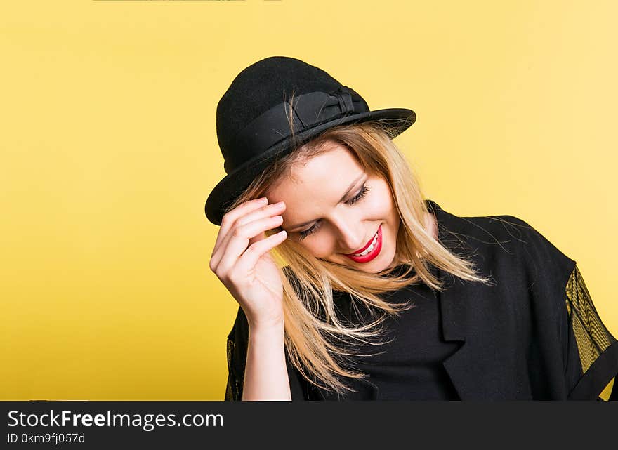 Portrait of a young beautiful woman with black hat and clothes in studio on a yellow background.