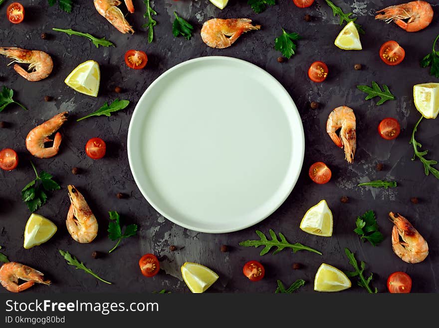 In the center of a dark textured background an empty gray plate, a mock-up. Around are scattered lemon, herbs, spices and shrimp. Beautiful photos from the top, mock up.